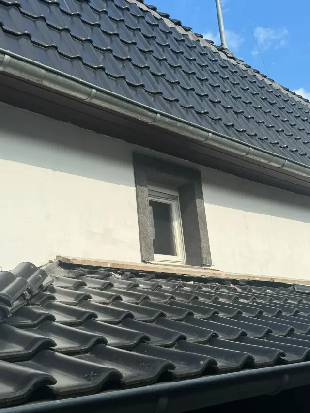 Szczyt dachu z ciemną dachówką i małym oknem w ciemnym obramowaniu, deska przy okapie