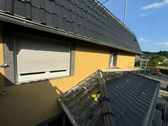 Żółta elewacja z roletą zewnętrzną, częściowo zdjęta dachówka i rusztowanie na dachu