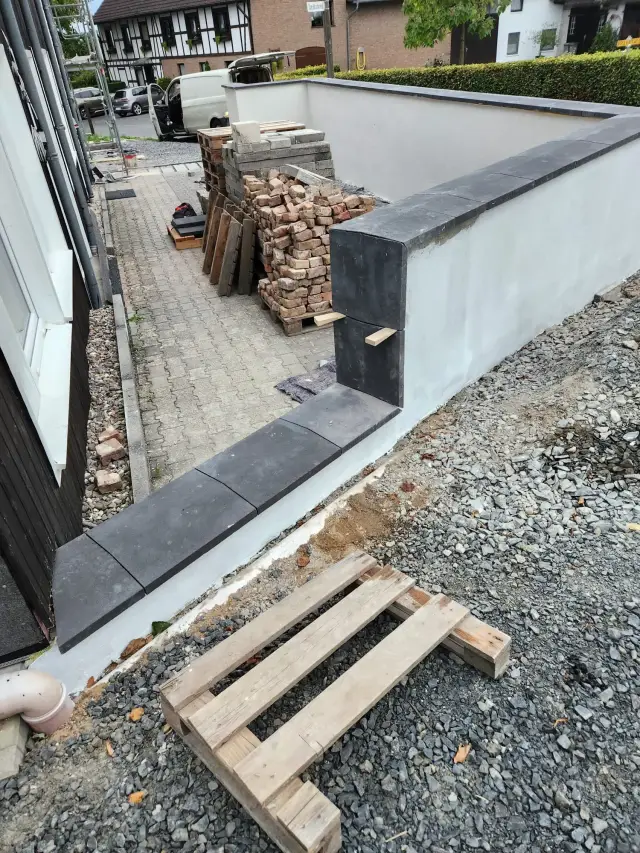 Murek z białym tynkiem, ciemne płyty na koronie i cegły na palecie przy podjeździe