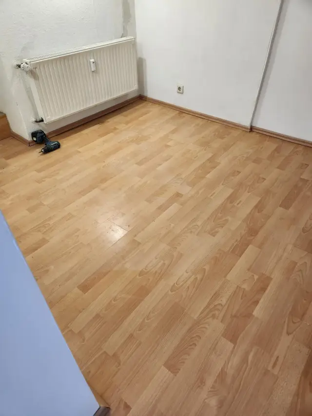 Pokój z podłogą laminowaną w jasnym odcieniu drewna, przy grzejniku