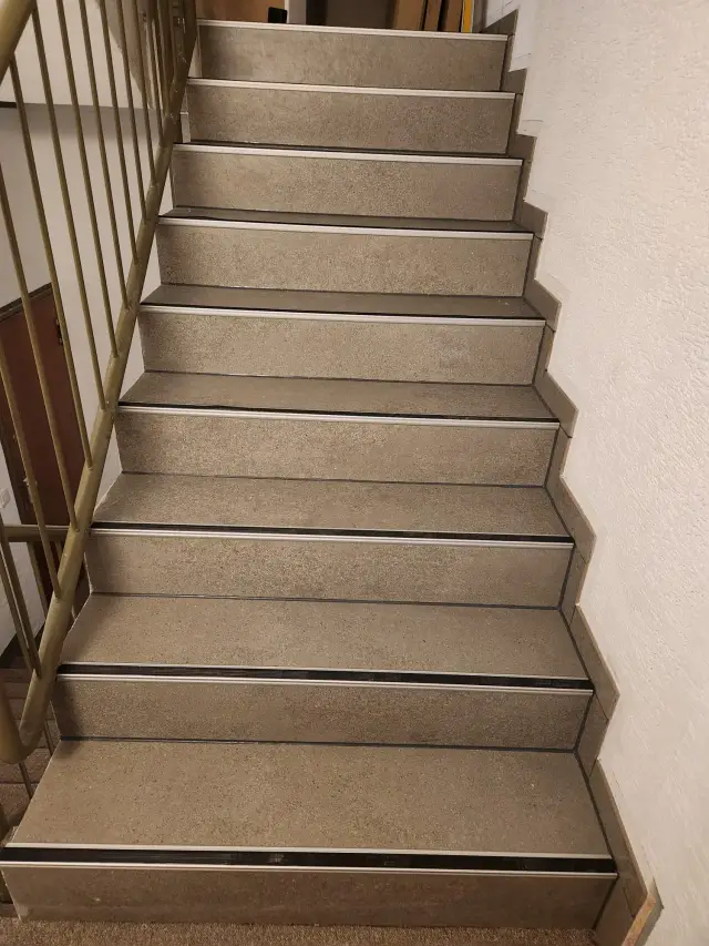 Klatka schodowa z szarymi stopniami, metalowymi nosami i jasną balustradą
