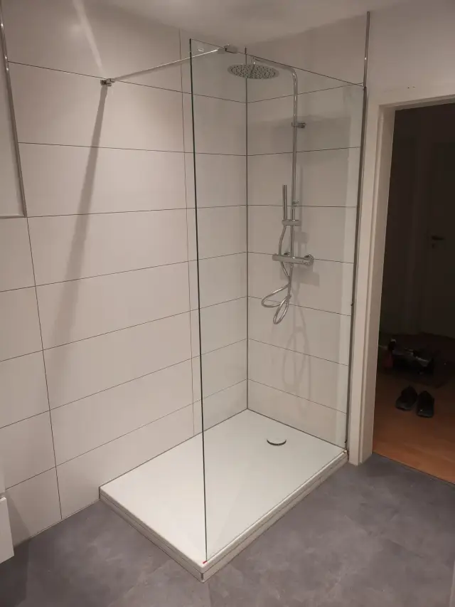Prysznic typu walk-in ze szklaną ścianką, białymi płytkami wielkoformatowymi na ścianie i brodzikiem