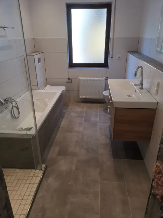 Łazienka z wanną, wiszącą szafką pod umywalkę i szarymi płytkami na podłodze