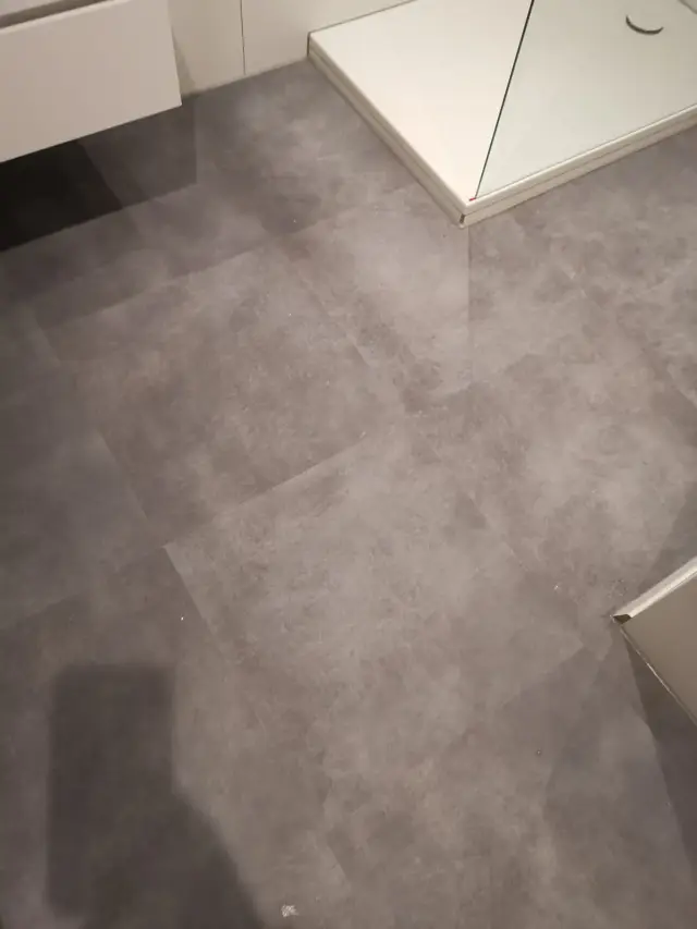 Zbliżenie na szarą podłogę winylową przy brodziku prysznicowym i szafce wiszącej