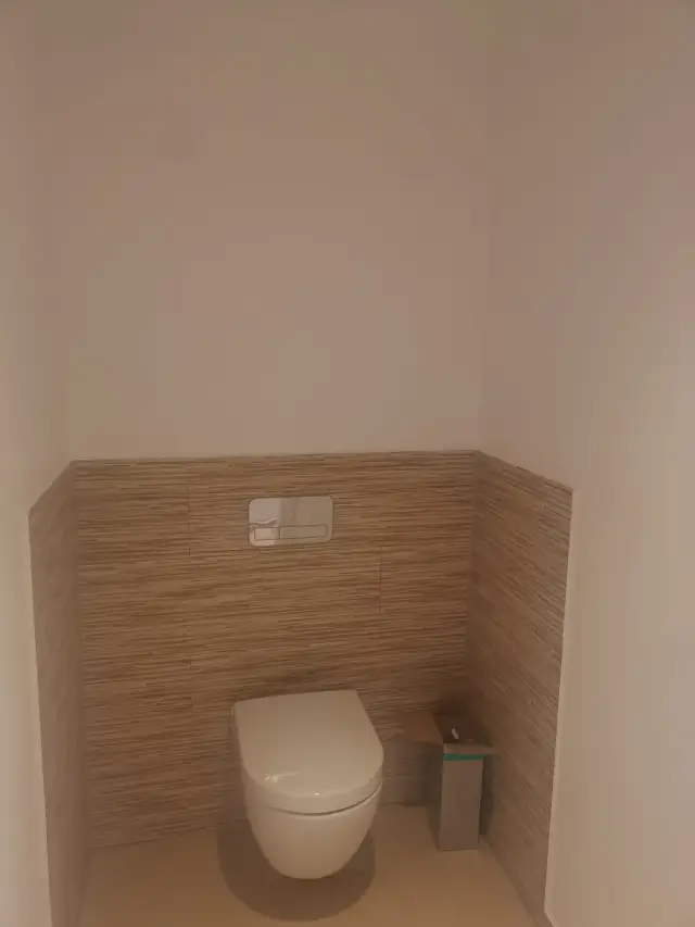 WC podwieszane w toalecie z pasową płytką na ścianie do połowy wysokości i przyciskiem spłuczki