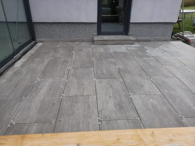 Taras z szarych płyt gresowych na regulowanych podporach przy przeszklonych drzwiach tarasowych