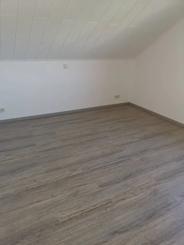 Pusty pokój na poddaszu z białym sufitem z listew i podłogą winylową imitującą drewno