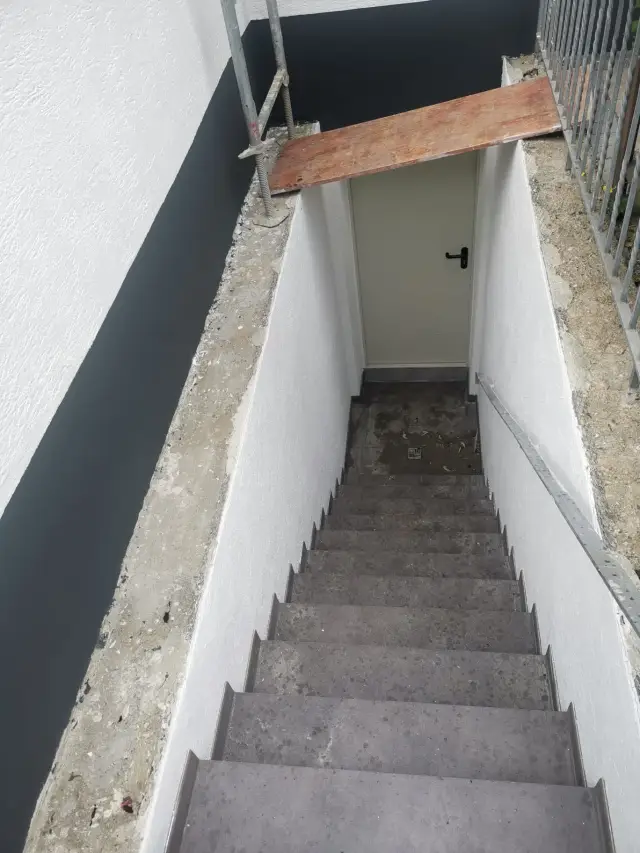 Schody zejściowe obłożone płytkami na stopniach, na wejściu w dole drewniana deska, w trakcie prac