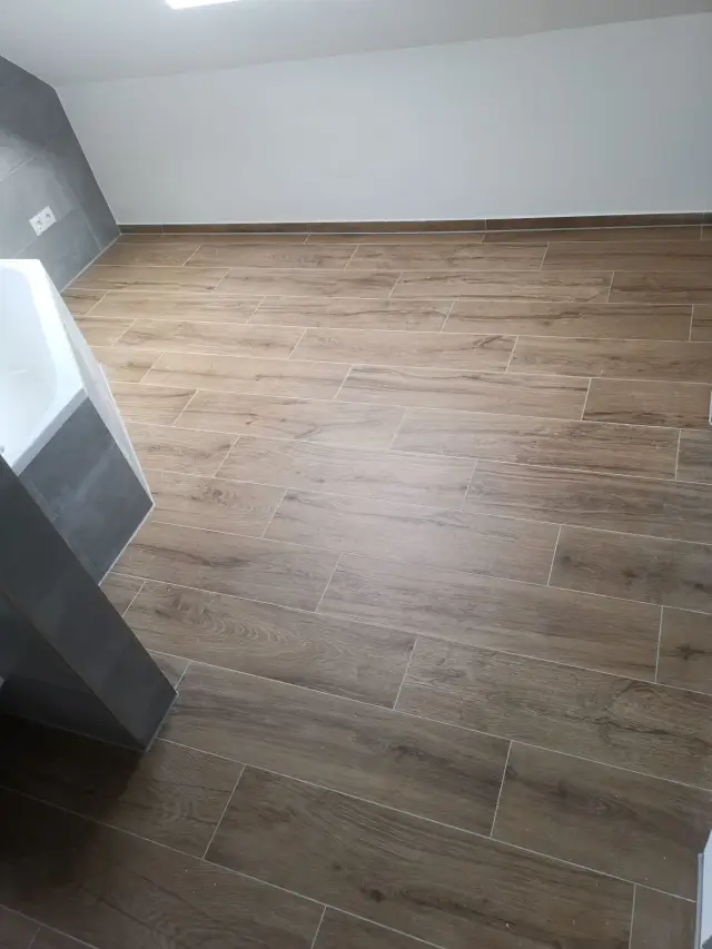 Podłoga z płytek drewnopodobnych na poddaszu, po lewej wanna obłożona szarą płytką
