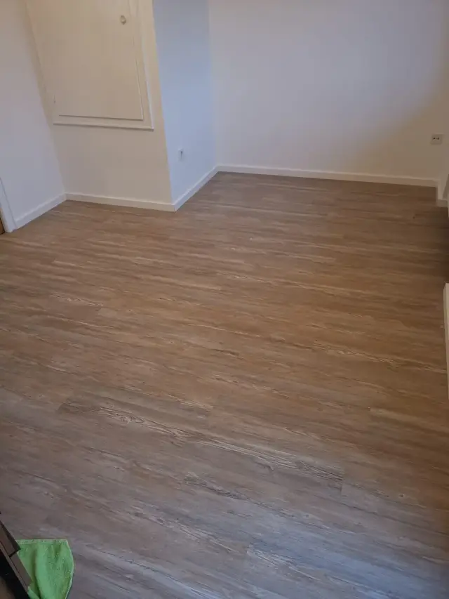 Pusty pokój z podłogą w imitacji drewna i białymi ścianami z listwami przypodłogowymi
