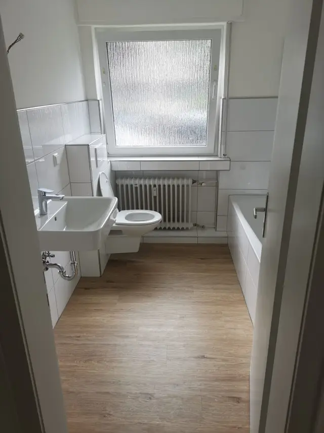 Łazienka z podłogą w imitacji drewna, białymi płytkami do połowy ściany i wanną