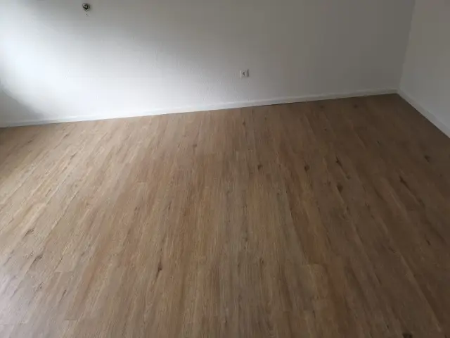 Pusty pokój z podłogą w imitacji drewna przy białej ścianie z gniazdkiem