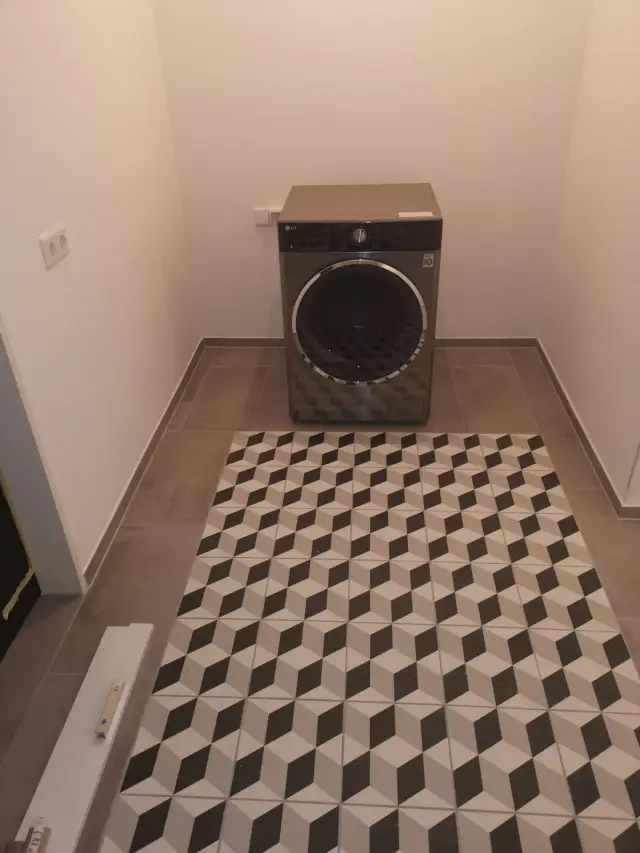 Pralnia z pralką i wzorzystymi płytkami na podłodze, ułożonymi w geometryczny wzór