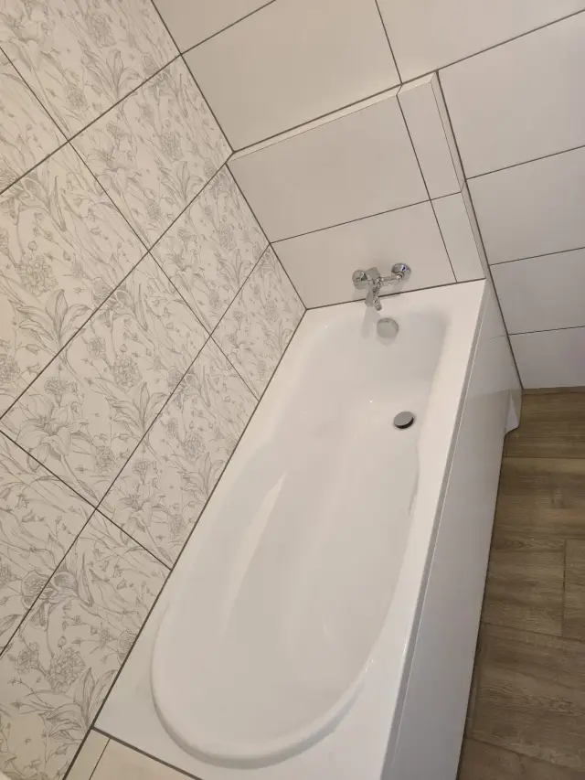 Wanna z baterią ścienną, płytki w roślinny wzór i ściana z białych płytek