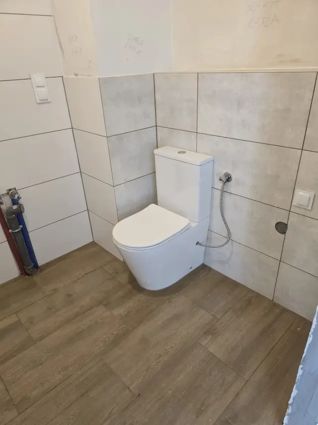 Łazienka z jasnymi płytkami wielkoformatowymi, WC kompakt i podłogą drewnopodobną
