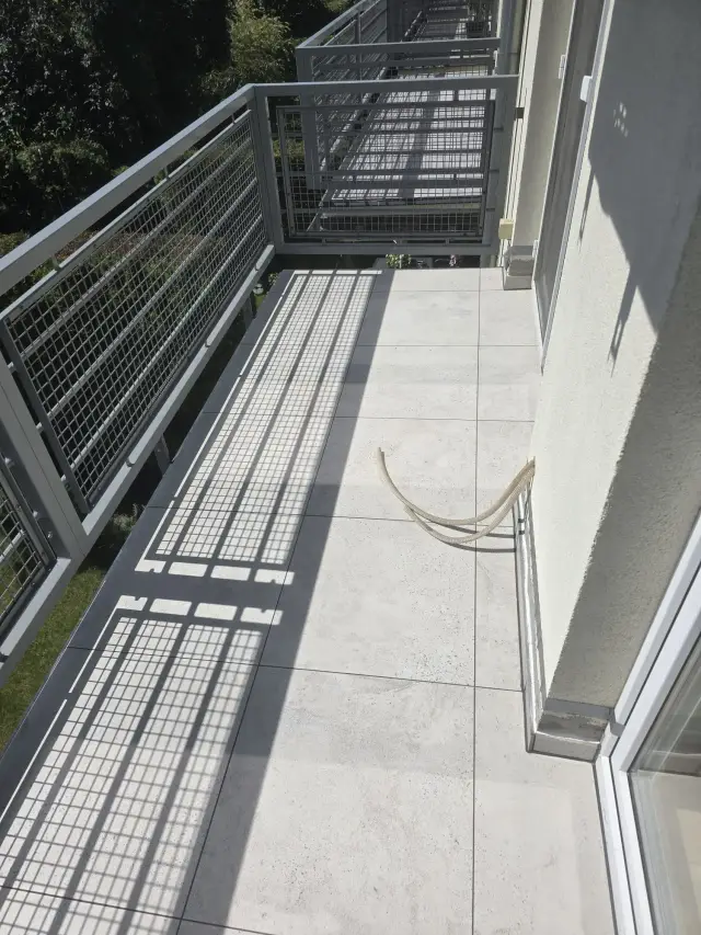 Wąski balkon z jasnym gresem i stalową balustradą z siatki