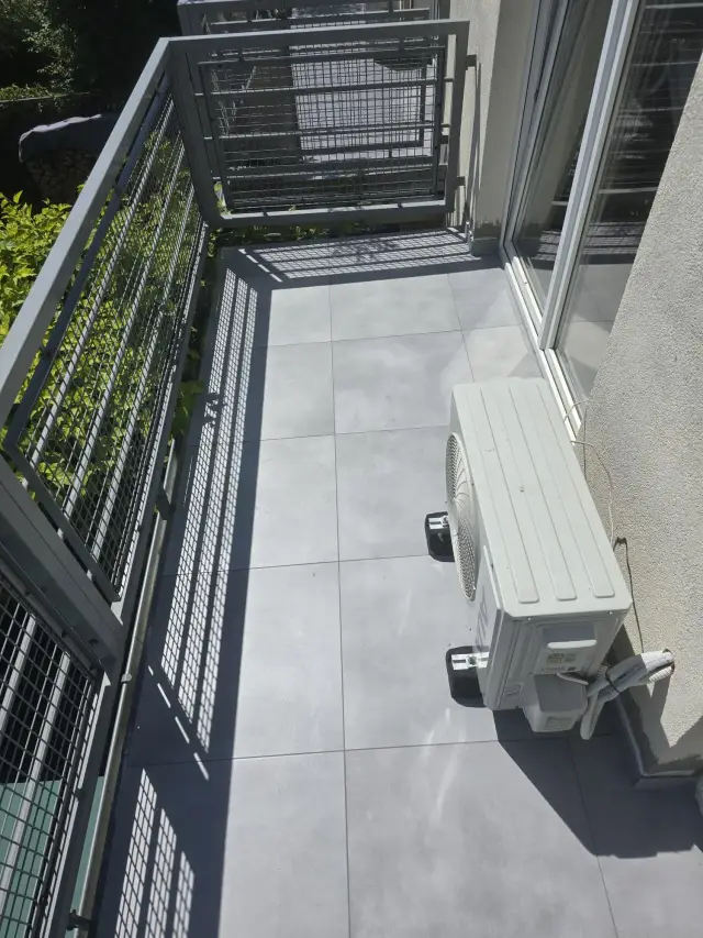 Balkon wyłożony szarym gresem wielkoformatowym z balustradą z siatki stalowej