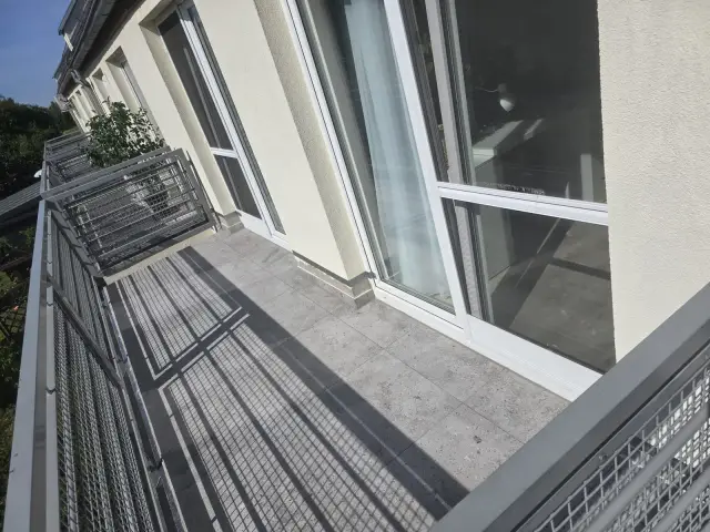 Balkon z ciemniejszym gresem wzdłuż przeszklonych drzwi balkonowych