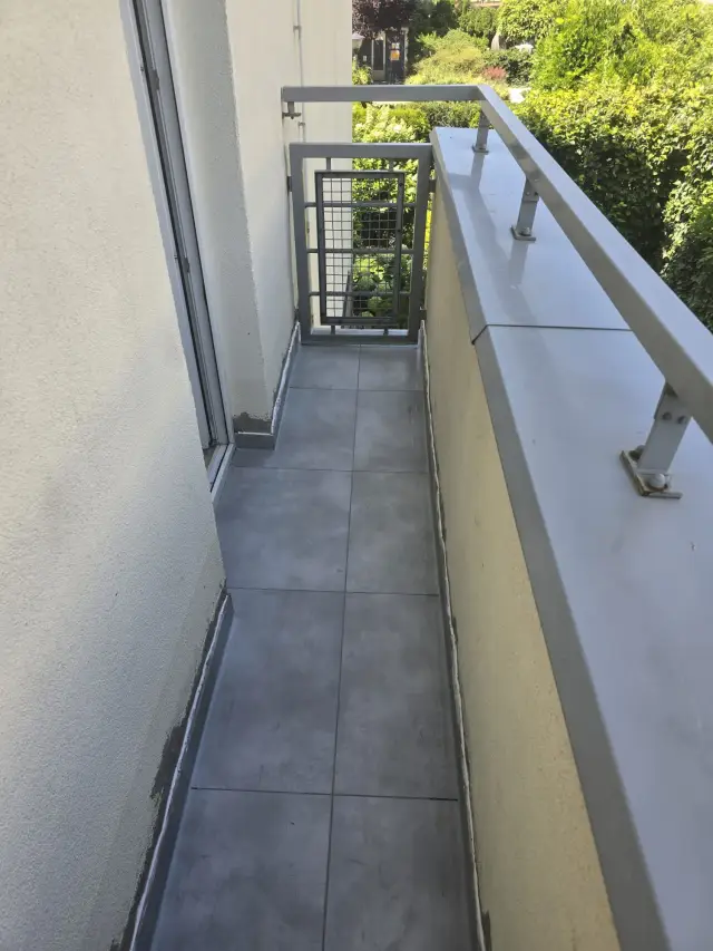Wąski balkon z ciemnym gresem i balustradą z obróbką blacharską