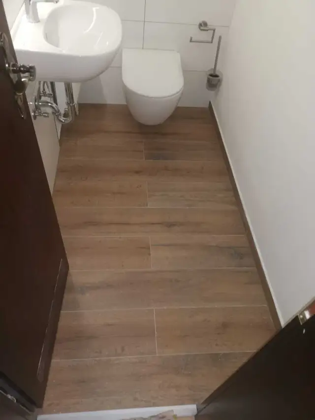 Toaleta z podwieszaną miską WC i drewnopodobnymi płytkami na podłodze