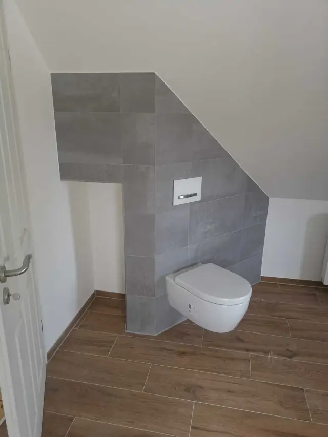 WC na poddaszu pod skosem dachu, z szarymi płytkami i podwieszaną miską
