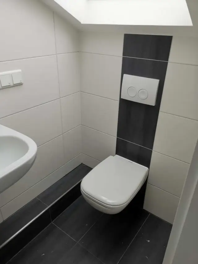 Małe WC pod oknem dachowym, białe płytki na ścianach, ciemne na podłodze