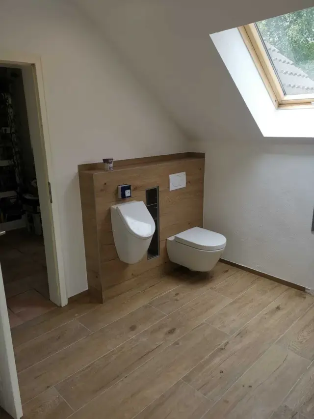 WC z pisuarem i miską podwieszaną, drewniana zabudowa i podłoga drewnopodobna