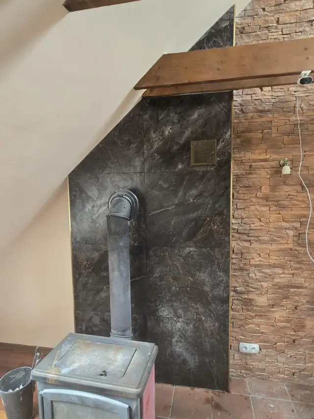 Piec kominkowy przed ścianą z ciemnych płytek imitujących marmur, z rurą kominową i kamieniem