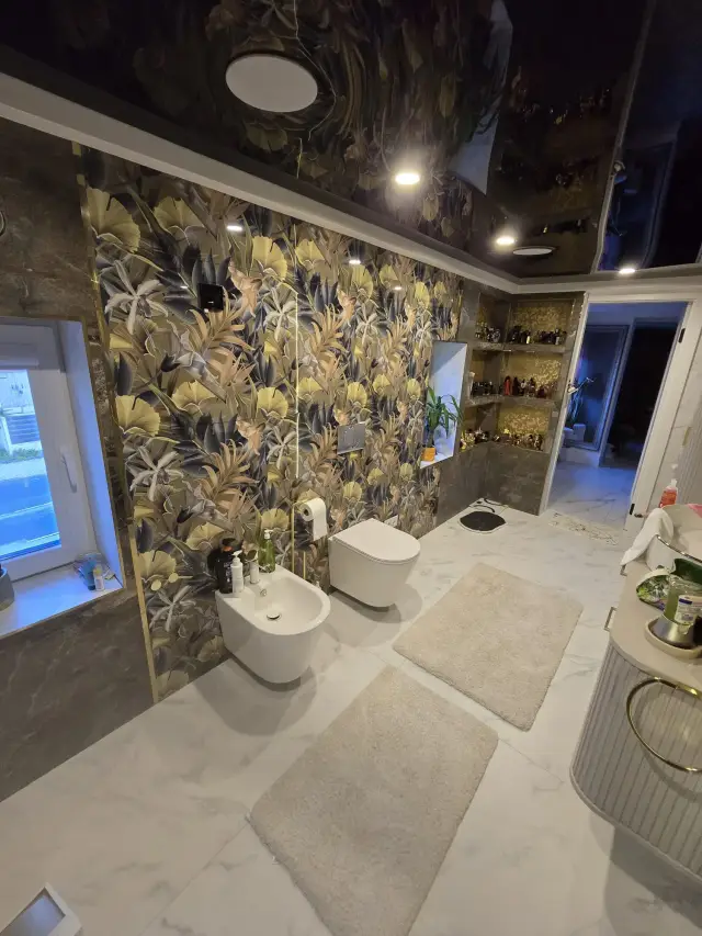 Łazienka z tapetą florystyczną na ścianie, WC podwieszane, bidet i jasna podłoga w imitacji marmuru