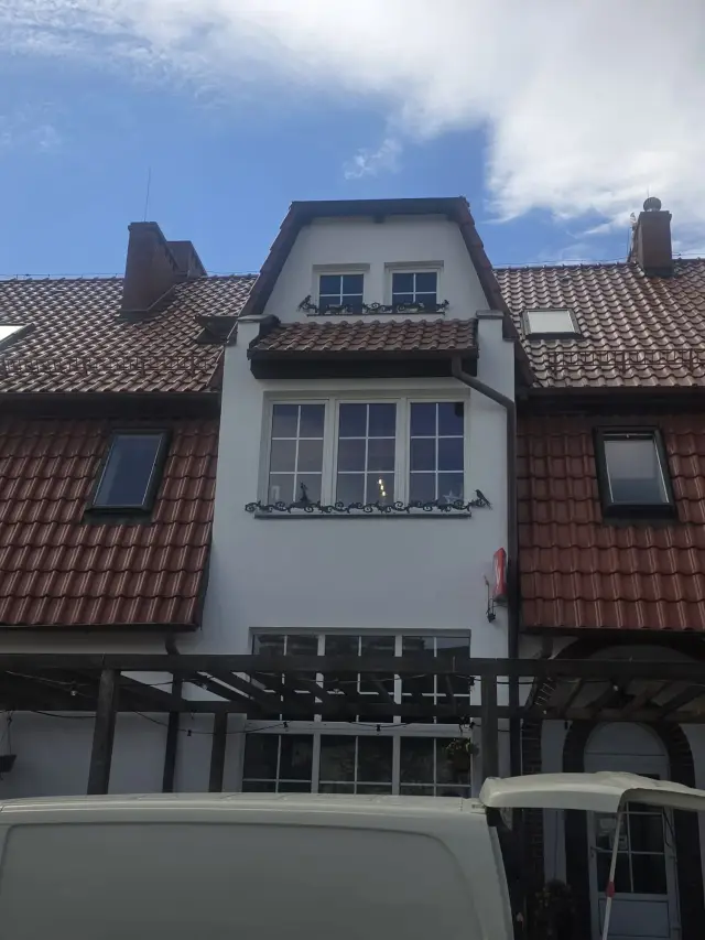 Elewacja szeregowca z ceramicznym dachem, lukarną i kutymi balkonikami okiennymi