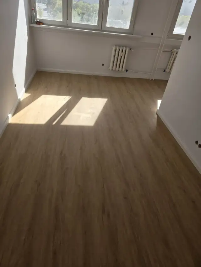 Pusty pokój z oknami, grzejnikiem i refleksami słońca na podłodze