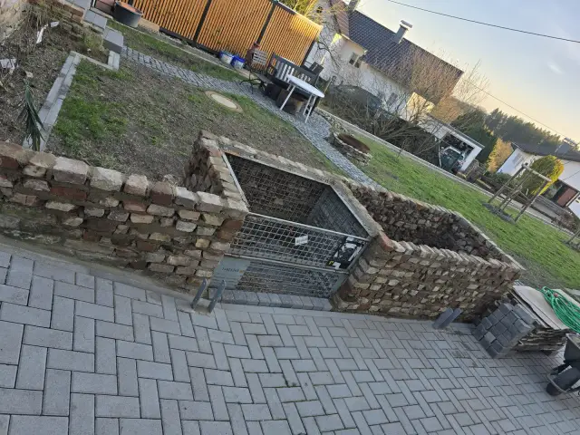 Ogrodowy murek z cegły przy metalowej kracie na tle kostki brukowej