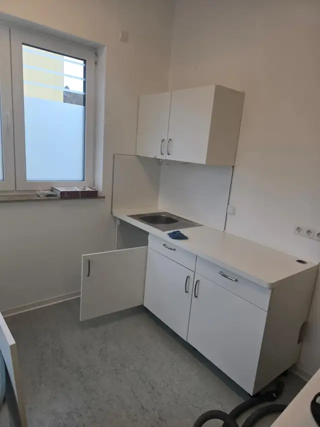 Mała kuchnia z białymi szafkami, zlewozmywakiem i szarą podłogą