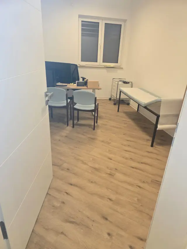 Gabinet z jasną podłogą winylową, krzesłami, biurkiem i łóżkiem do badań