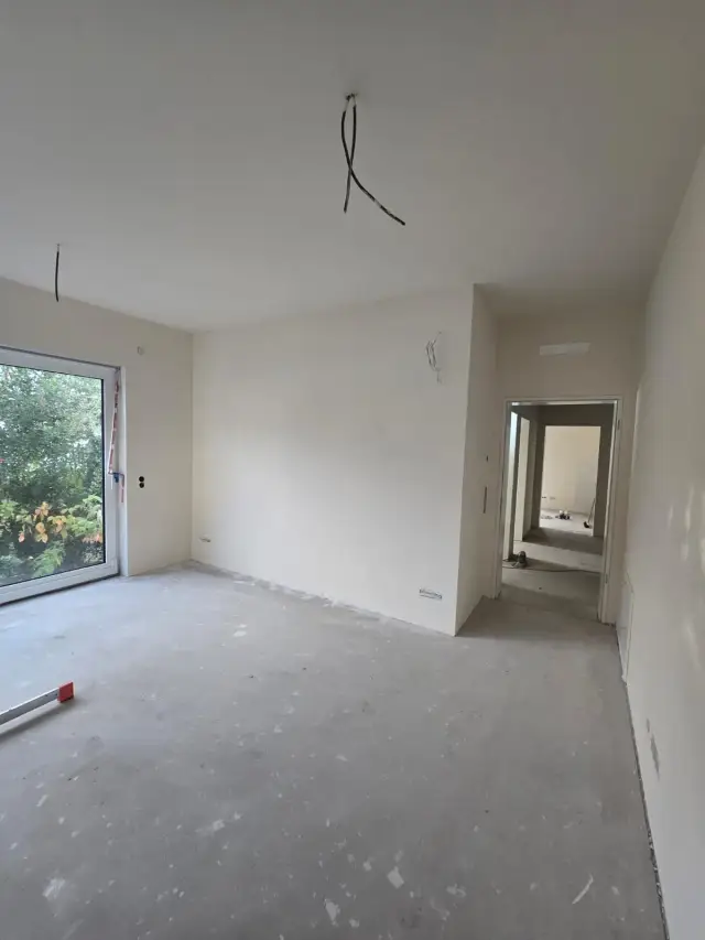 Pomieszczenie bez wykończeń, białe ściany, betonowa posadzka i okno na ogród