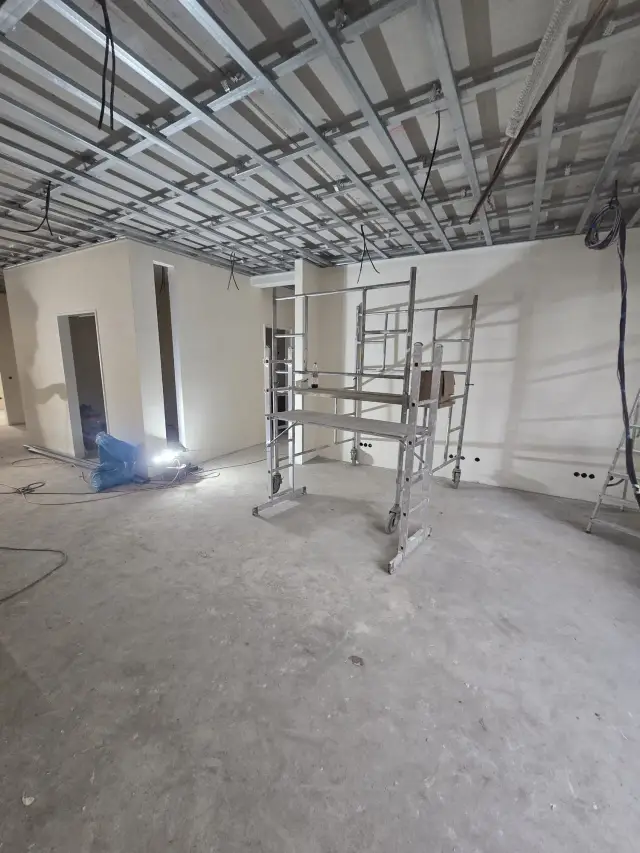 Pomieszczenie z konstrukcją sufitu podwieszanego, rusztowaniem i gołą posadzką betonową